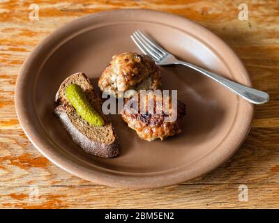 Zwei gebratene russische Kotleta (panierte Hacksteaks), Roggenbrot und Gurke auf Keramikplatte auf alten Holztisch in der Küche Stockfoto