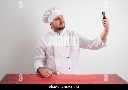 Porträt des jungen männlichen Koch in weißer Uniform unter Selfie-Fotografie posiert auf einem weißen isolierten Hintergrund Stockfoto