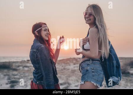 Zwei junge Frauen gehen zum Meer entlang des sandigen Ufers zurück Blick langsam Stockfoto
