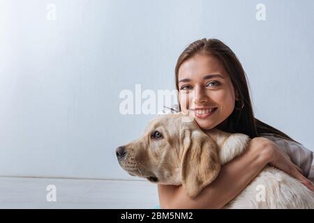 Schöne Frau lächelt vor der Kamera, während umarmt goldenen Retriever auf grauem Hintergrund Stockfoto