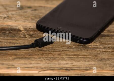 Nahaufnahme von schwarzem Smartphone-Akku mit einem USB-Kabel auf Holztisch mit Kopierraum . Stockfoto