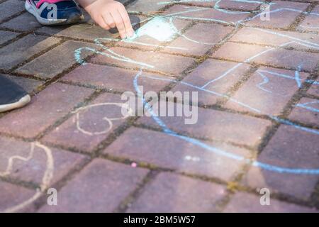 Mädchen sitzt auf Beton Asphaltstraße., auf Steinweg. Kinder Malerei Linien, Zahlen mit Kreide auf Asphalt. Selektive Focus.Little girl Hände Malerei Stockfoto