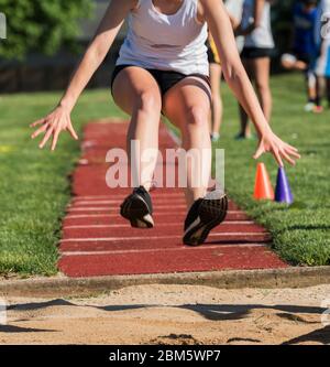 Ein Mädchen aus der High School ist im Dreisprung mit einem Leichtathletik-Wettkampf dabei und landet in der gesunden Grube. Stockfoto