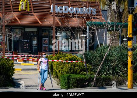 Frau mit Krücken mit schützender Gesichtsmaske steht vor geschlossen für normale Geschäfte McDonald's Fast Food Restaurant erlaubt nur Drive-in oder Drive-Thru Essen zum Mitnehmen aufgrund der Ausbreitung der Coronavirus Pandemie von Covid-19 in Sofia, Bulgarien seit April 2020 Stockfoto