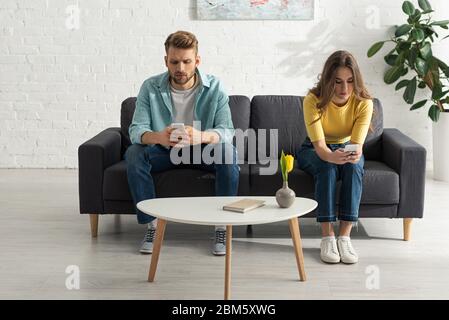 Junges Paar mit Smartphones auf der Couch in der Nähe Buch auf Couchtisch Stockfoto