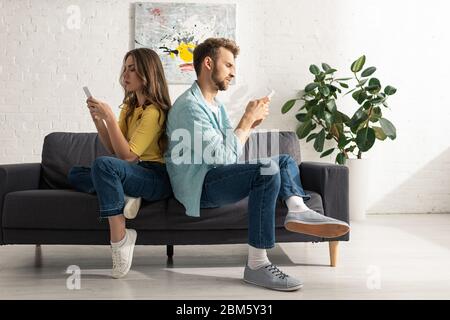 Seitenansicht des Paares mit Smartphones während es sich auf dem Sofa zurücklehnen Stockfoto