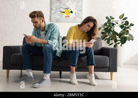 Junges Paar mit Smartphones, während auf der Couch zu Hause sitzen Stockfoto