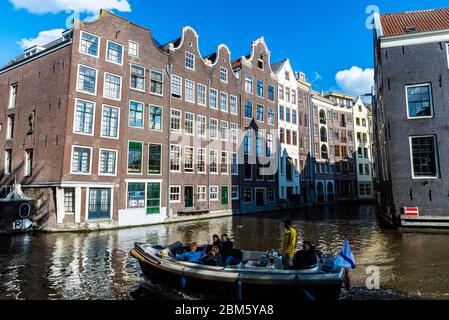 Amsterdam, Niederlande - 7. September 2018: Alte traditionelle schiefe Häuser entlang eines Kanals mit Menschen, die in einem Boot in der Altstadt von Amsterdam, N Stockfoto