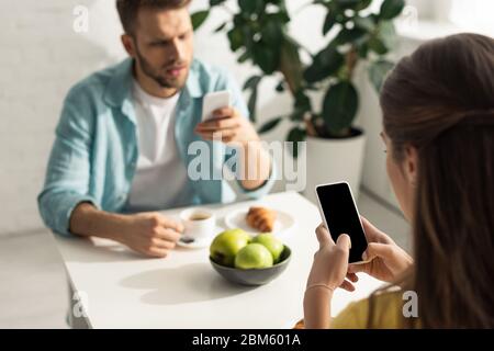 Selektiver Fokus der Frau mit Smartphone in der Nähe Freund beim Frühstück chatten Stockfoto