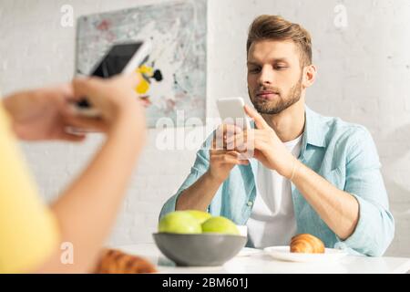 Selektiver Fokus des Mannes mit Smartphone in der Nähe Freundin beim Frühstück in der Küche Stockfoto