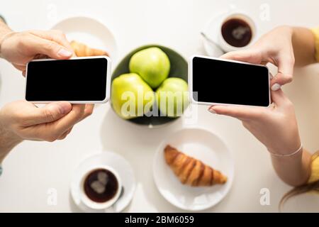 Draufsicht auf das Paar mit Smartphones in der Nähe des Frühstücks auf dem Tisch Stockfoto