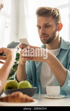 Selektiver Fokus von süchtig Paare, die Smartphones in der Nähe von Kaffee und Croissant auf dem Tisch Stockfoto