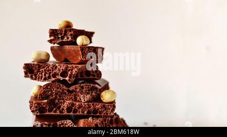 Schokolade auf weißem Hintergrund, isoliert. Poröse Schokolade mit Nüssen, Textur, Nahaufnahme. Freier Platz für Text. Stockfoto