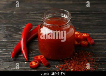 Chili Pfeffer und Glas mit Sauce auf Holzhintergrund Stockfoto