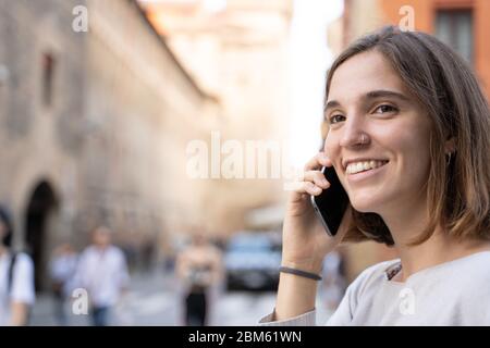 Junge Frau mit einer halben Mähne und einer durchbohrten Nase lächelnd und mit ihrem Handy auf der Straße sprechend Stockfoto