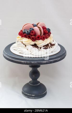 pawlova-Kuchen mit Schlagsahne, frischen Erdbeeren, Himbeeren, Blaubeeren und rosa Makronen. Einfarbiger weißer Hintergrund. Kopierbereich. Stockfoto