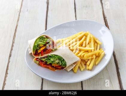 Pita-Brot-Pfannkuchen, gefüllt mit Fleisch, Salat, rotem Pfeffer und Bratkartoffeln auf einem weißen Teller, auf einem Holztisch. Nahaufnahme. Stockfoto