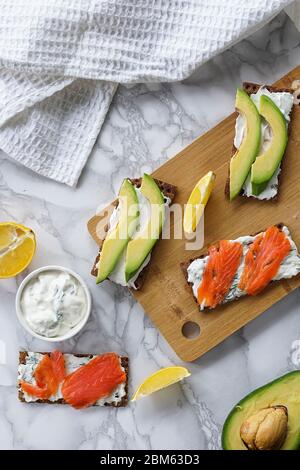 Frühstück am Morgen, zartes hausgemachtes Weichkäse auf Crackern mit geräucherter Forelle und Avocado Stockfoto