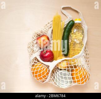 Lieferung von Lebensmitteln. Öko-Beutel Netz mit frischen Lebensmitteln: Öl, Spaghetti, Apfel, Orang, Gurke, Waren für die Spende während der Quarantäne. Stockfoto