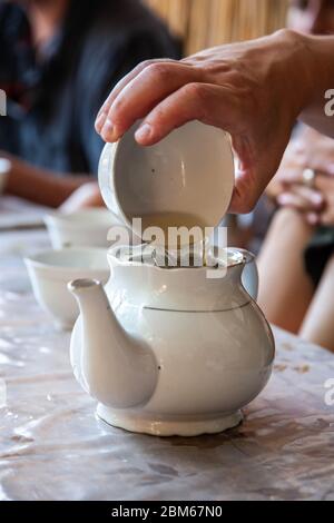 Heißer Tee wird aus einer Tasse in eine Teekanne gegossen. Traditionelle Teezeremonie. Stockfoto