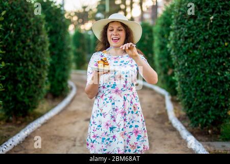 Ziemlich lustige Frau, die den Kuchen im Park isst. Essen, Ernährung, ungesunde Lebensmittel und süße Konzept. Zuckersucht. Stockfoto