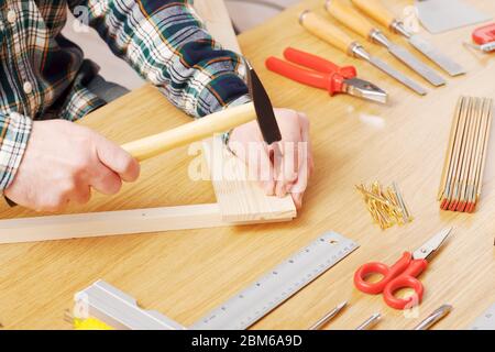 Zimmermann die Hände nah, er hämmert einen Nagel in eine Holzplanke auf einer Werkbank, DIY und Hobby-Konzept Stockfoto