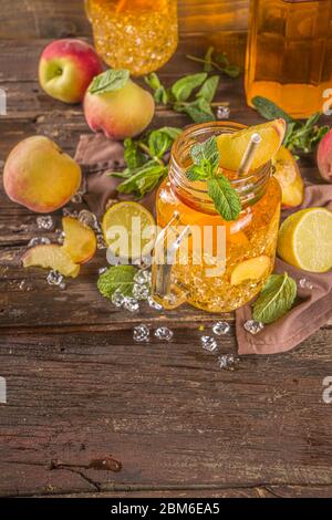 Frischer hausgemachter Pfirsich-Süßer Tee mit Minze- und Zitronenscheiben, sommerlicher kalter Fruchtdrink. Holzhintergrund mit frischem Pfirsich, Kopierraum Stockfoto