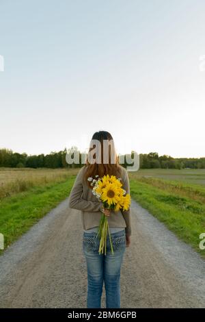 Rückansicht der jungen asiatischen Frau mit Sonnenblumen hinter zurück in der Natur Stockfoto