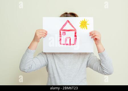 Kinderhände halten Bild von Haus mit Sonne, die ihr Gesicht auf gelbem Hintergrund bedeckt. Kinder mit gezogenem Haus. Stockfoto