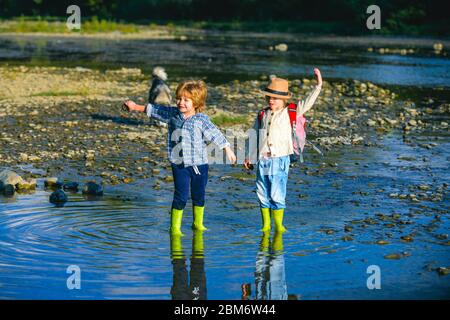 Kinder werfen Steine. Zwei kleine Geschwister und Schwester spielen an warmen und sonnigen Sommertagen in einem Fluss oder See. Kinder werfen Stein in Wasser. Chi Stockfoto