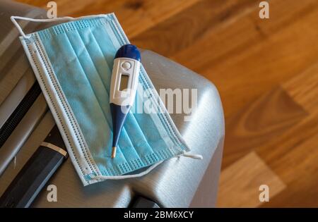 Nahaufnahme einer medizinischen Gesichtsmaske und Thermometer auf dem Koffer für Geschäftsreisen oder Urlaub während der Coronavirus-Epidemie Stockfoto