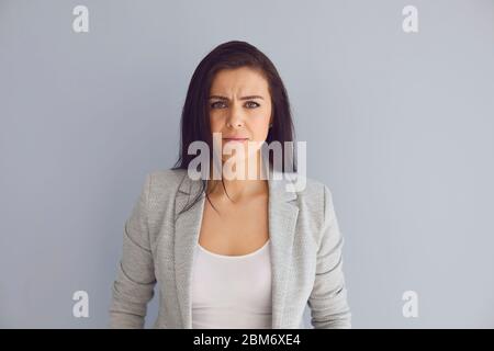 Junge beschäftigte Unternehmerin in stilvollem Outfit Blick auf Kamera und Stirnrunzeln mit ernsten Problemen, während vor grauem Hintergrund stehen Stockfoto