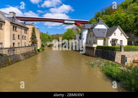 Fluss Alzette in Pfaffenthal, Luxemburg, mit Häusern am Flussufer. Im Hintergrund Vauban Tower und Grand Herzogin Charlotte rote Brücke. Stockfoto