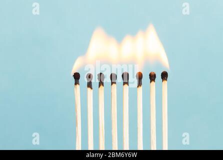 Acht Streichhölzer brennen vor einem schlichten blauen Hintergrund. Stockfoto