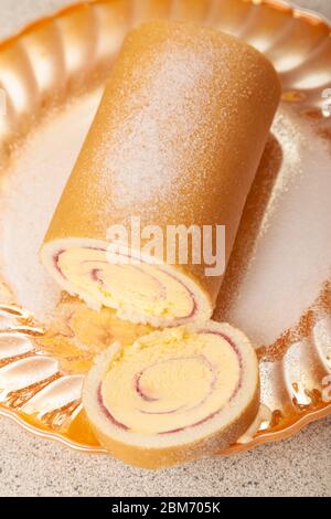 Eine in Scheiben geschnittene Arctic Roll gefrorene Wüste, die mit Gießzucker auf einer Goldplatte bestäubt wurde. Stockfoto