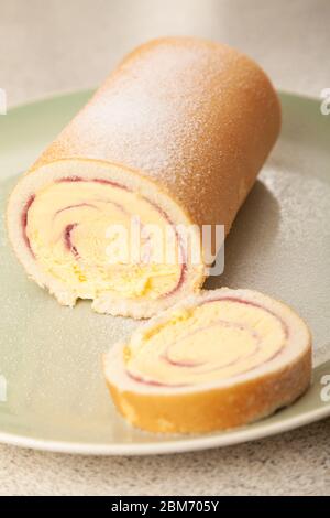 Eine in Scheiben geschnittene Arctic Roll gefrorene Wüste, die mit Zucker auf einer grünen Platte bestäubt wurde. Stockfoto