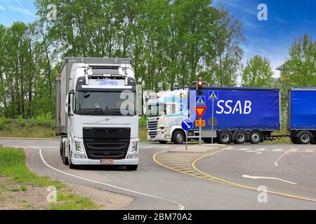 Zwei kundenspezifische weiße Volvo und Scania Lastwagen von Transport K. Lindholm & Co schleppen Fracht auf Autobahn Kreuzung. Raasepori, Finnland. 24.Mai 2019. Stockfoto