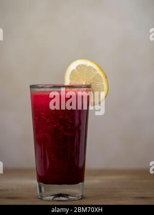 Ein Glas mit rotem Rübensaft, verziert mit einer Zitronenscheibe auf Holzfläche und vor braunem Hintergrund - gesundes Getränkekonzept mit viel Copy-sp Stockfoto