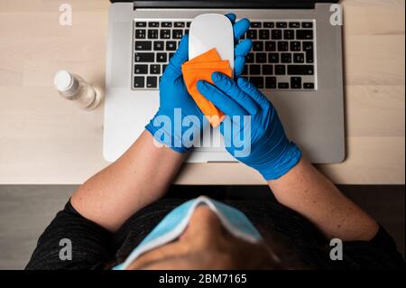 Unkenntlich Frau mit Schutzmaske Reinigung und Desinfektion einer Maus. Reinigen der Oberflächen von Notebook-Computern von Viren, Mikroben und Schmutz Stockfoto