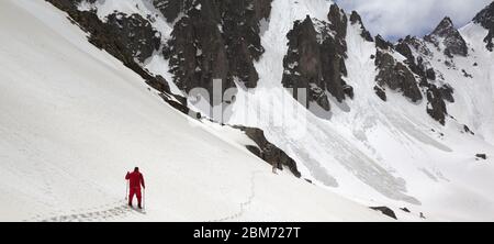 Snowy Mountains mit Lawine Spuren, sunlit bewölkter Himmel, Wanderer in Rot mit Skistöcken und Hund auf schneebedeckten Hang in sonniger Tag. Türkei, Kachkar Berge, Stockfoto