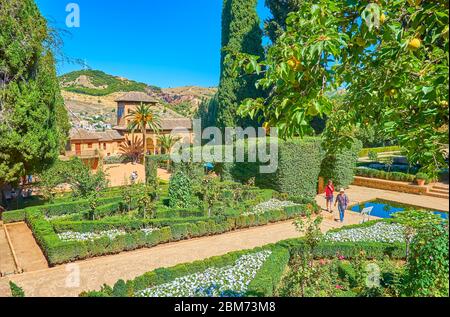 GRANADA, SPANIEN - 25. SEPTEMBER 2019: Der malerische Partal-Garten der Alhambra mit Topiarpflanzen, bunten Blumen in Blumenbeeten, Pool und Partal-Palast Stockfoto