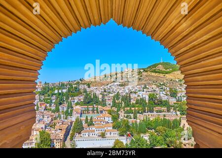 Der geschnitzte Bogen im Mudejar-Stil des Palastes Partal in Alhambra eröffnet den Blick auf die Festungsmauern und Albaicin (Albayzin), das hügelige Granada Stockfoto