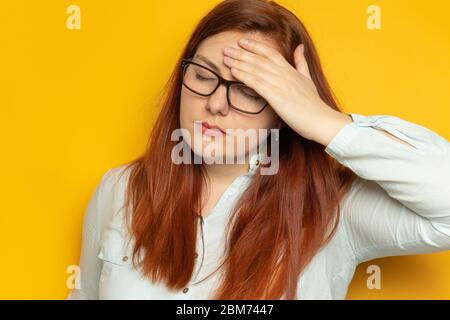Arbeiter junge Frau in Hemd und Brille mit Kopfschmerzen auf gelben Wand Hintergrund. Stress, Müdigkeit Menschen Konzept. Halten Sie die Hände auf dem Kopf Stockfoto