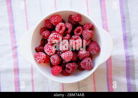 Gefrorene Himbeeren in einer weißen Schüssel auf einem traditionellen Textiltuch. Vegetarisches und gesundes Konzept. Stockfoto