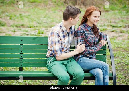 Flirting junges Paar in karierten Hemden auf einer Bank im Park sitzen Stockfoto