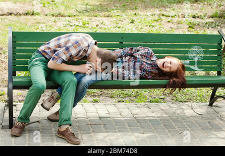 Flirten Lachen und Spaß haben junge Paar in karierten Hemden sitzen auf einer Bank im Park Stockfoto