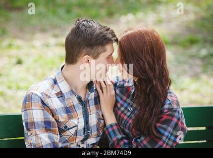 Flirting junges Paar mit geschlossenen Augen in karierten Hemden auf einer Bank im Park sitzen Stockfoto