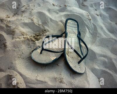 Ein Paar Bambussandalen liegen auf dem Sand an einem Strand in Italien. Konzept von Urlaub und Entspannung am Meer. Stockfoto