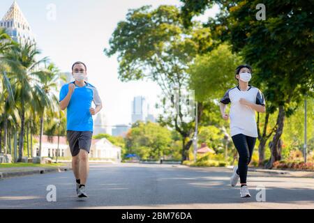 Asiatische junge Paar Frau und Mann sind Joggen und exciseing im Freien in Stadtpark und tragen Schutzmaske im Gesicht für Aufenthalt in fit während Covid-19 pa Stockfoto