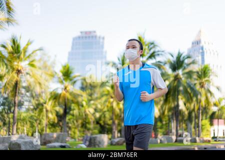 Asiatische junge Mann joggen und exciseing im Freien im Stadtpark und tragen Schutzmaske auf Gesicht für Aufenthalt in der fit während Covid-19 Pandemie in Bangkok Stockfoto
